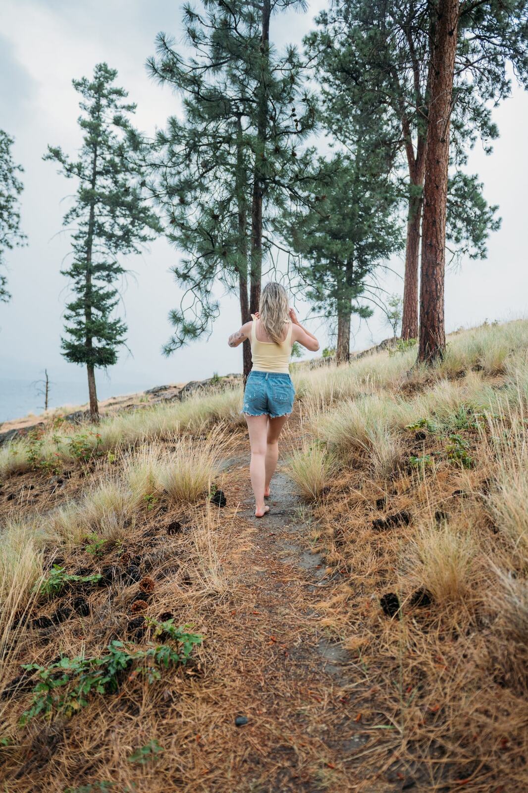 Sophia by the Lake portraits story frame 12: A multi-outfit Okanagan location session with water, trees, shoreline, denim and red swimwear woven into a summer portrait story.