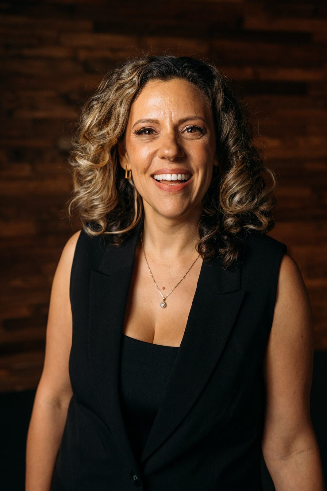 Trisha Miltimore corporate story frame 10: Personal-brand portraits for Trisha Miltimore in Kelowna, moving from clean business profile images into darker wood-wall portraits with black wardrobe and confident brand range..