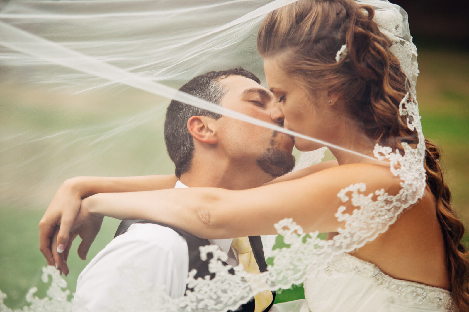 Bride and groom kissing through a wind-blown veil