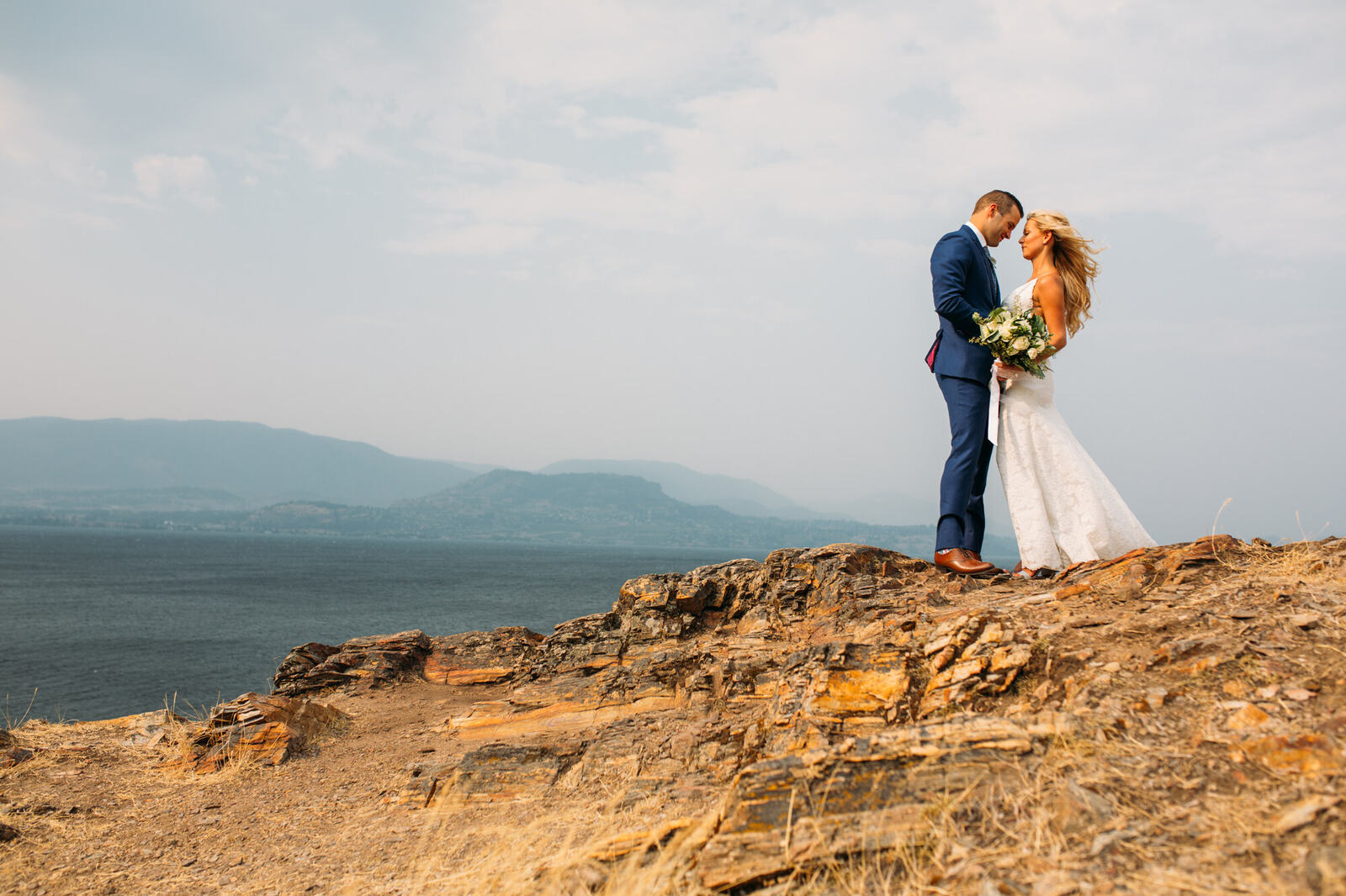 Bride and groom standing together above a lake landscape